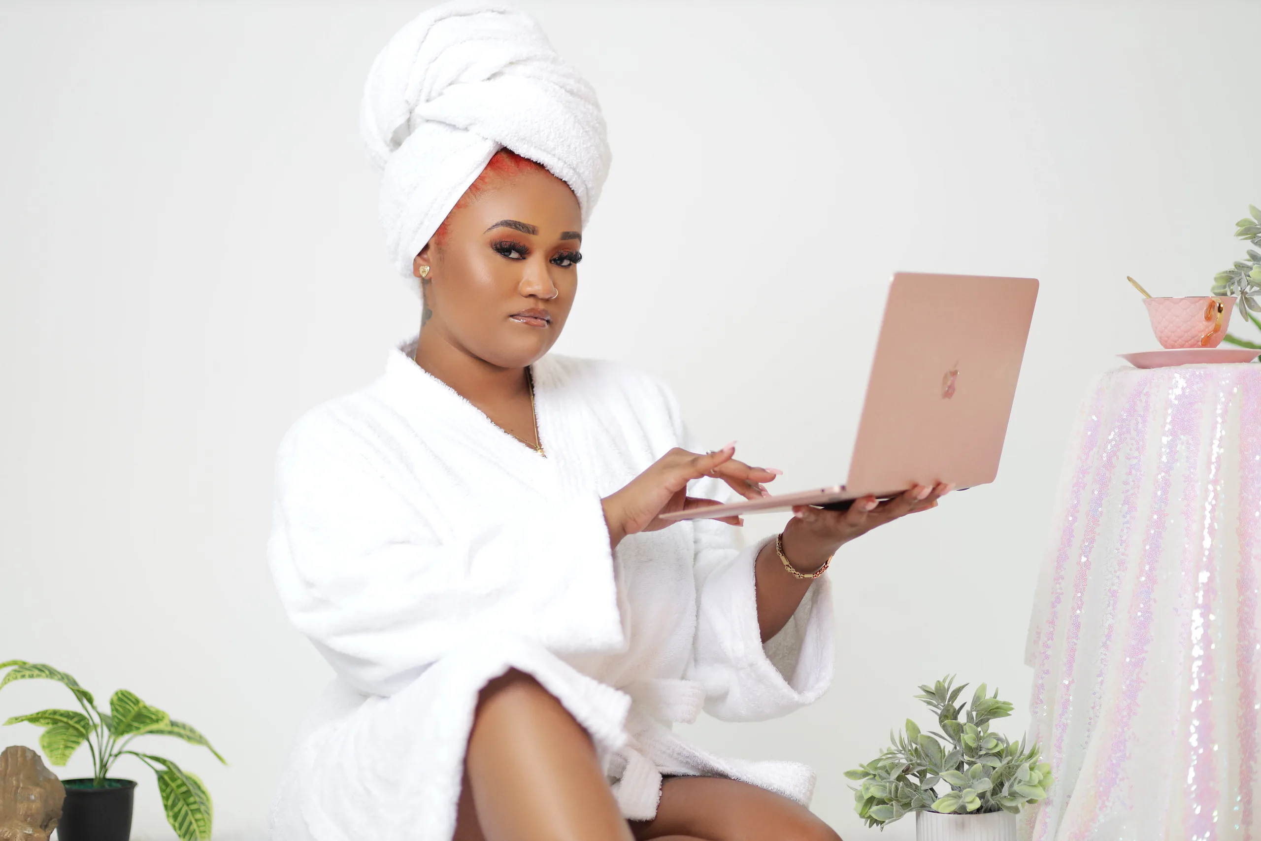 Branding portrait of a woman in a white robe using a laptop in a styled pastel photo set