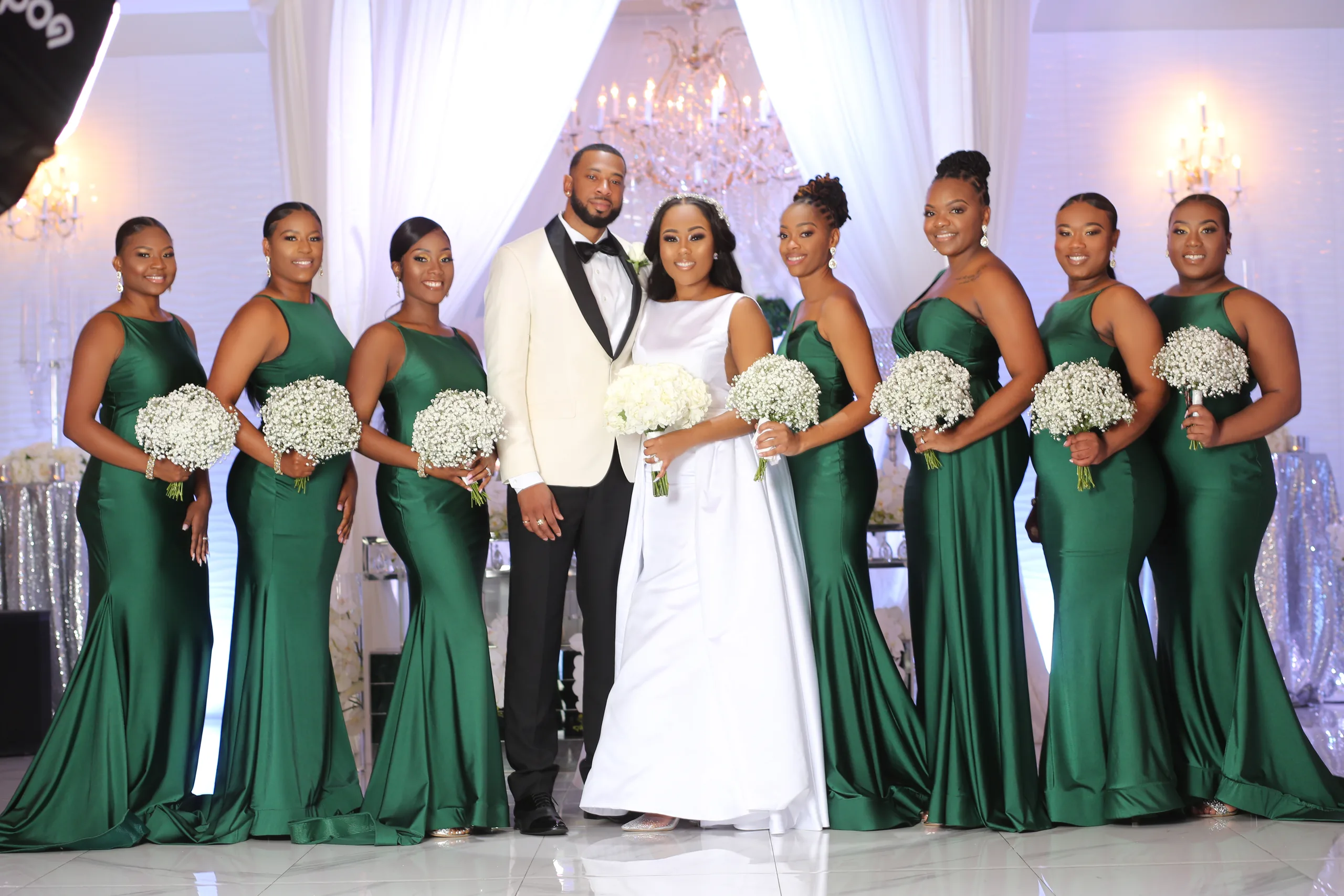 Bride and groom posing with bridesmaids in emerald green gowns at an elegant wedding reception